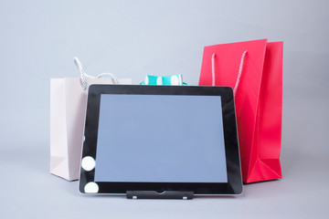 Online shopping concept. Close-up tablet mockup with white screen with bright gift bags on gray background.