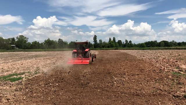 Red tractor tilling soil in a barren landscape