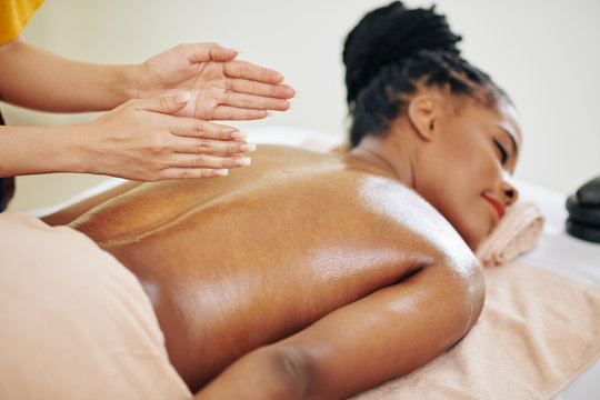Close-up image of therapist massaging back of pretty young Black woman with organic oils