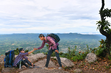 A young man was pulling his friend up on a high cliff.