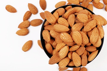 Group of almonds inside and outside bowl isolated on white.