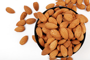 Group of almonds inside and outside bowl isolated on white.