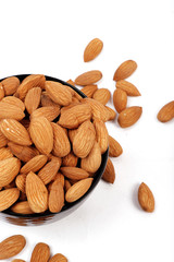 Group of almonds inside and outside bowl isolated on white.