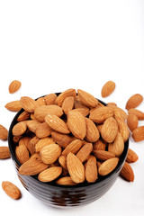 Group of almonds inside and outside bowl isolated on white.