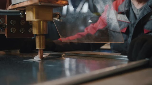 A professional worker behind protective glass works with a metalworking machine. Craftsman, miller or engineer. Sparks fly in the process of work, close-up. Slow motion