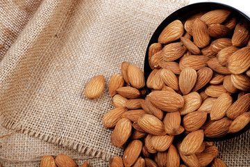 Group of almonds inside and outside bowl isolated on white.