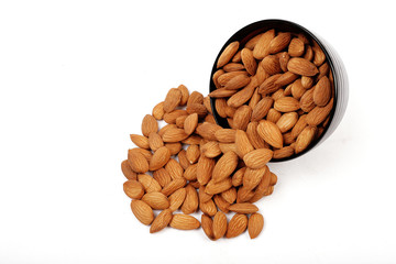 Group of almonds inside and outside bowl isolated on white.