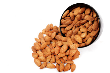 Group of almonds inside and outside bowl isolated on white.