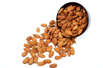 Group of almonds inside and outside bowl isolated on white.