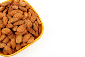 Group of almonds inside and outside bowl isolated on white.