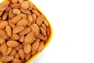 Group of almonds inside and outside bowl isolated on white.