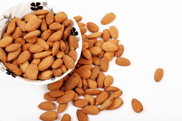 Group of almonds inside and outside bowl isolated on white.