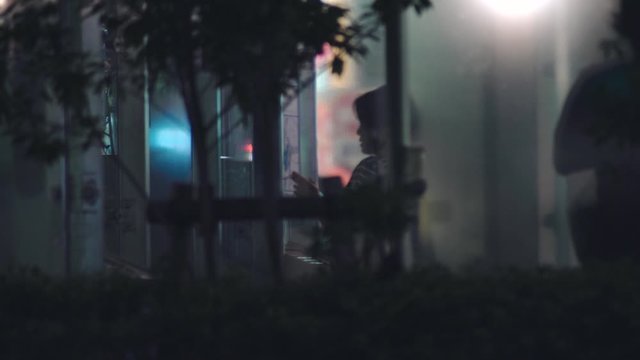 Japanese Woman Smoking A Puff Of Cigarette In The Designated Smoking Area While Browsing On Phone at Night In Kamata