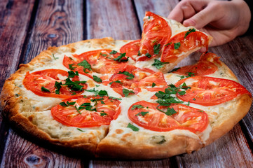 classic Italian pizza on a wooden table close-up, hand takes a slice of pizza