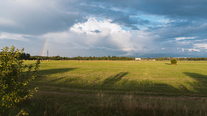 Fototapeta na wymiar Field for harvesting hay. A bunch of cloudy sky with a rainbow. Beautiful evening landscape.