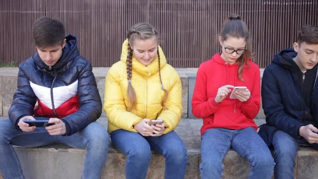 Teenage friends spending time together in city streets in spring, discussing interesting topics and browsing on phones