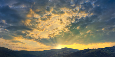 Fototapeta premium Mountains with beautiful sunset with the bright setting sun breaking through the clouds