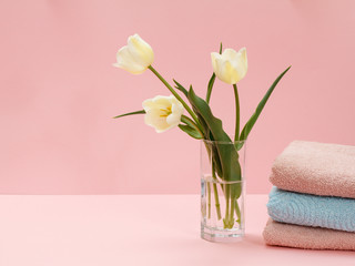 Bouquet of yellow tulips in vase with towels on a pink background.