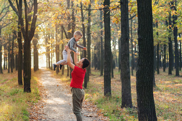 Fototapeta premium Beautiful woman throws her little kid up in the air in autumn park