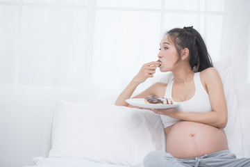 Obraz na płótnie Canvas beautiful young pregnant woman holding sweet donut in her hand. expectation of the child, pregnancy and motherhood. healthy and unhealthy eating concept, diet. Junk food. soft focus background
