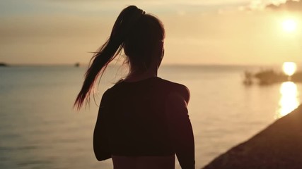 Athletic woman with waving hair running on beach at dramatic sun. Medium shot on RED camera - Powered by Adobe