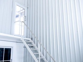 Inside white modern cutting-edge shipping container construction office building with white iron staircase leads up to the glass door on the upper floor.