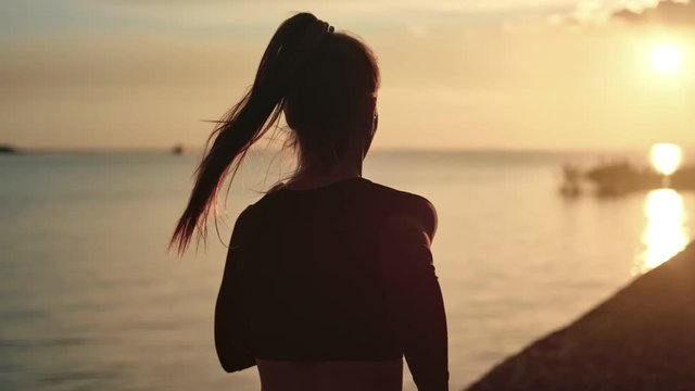 Athletic woman with waving hair running on beach at dramatic sun. Medium shot on RED camera - Powered by Adobe