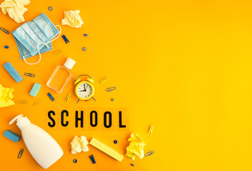 Text SCHOOL on yellow background with school supplies, protective face mask and sanitizer antiseptic. Back to school. New normal. School quarantine concept