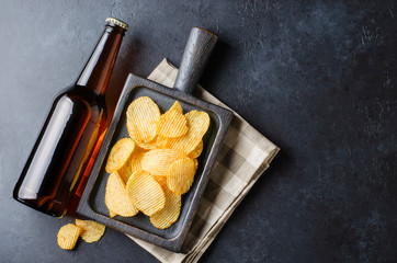 Beer in dark glass bottles and salty snacks. Dark concrete background. Top view. Free space for text.