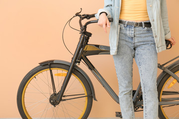 Beautiful young woman in jeans clothes and with bicycle near color wall