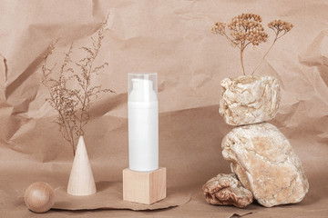 White blank cosmetic tube with cream, serum or other cosmetic product, stones, geometric shape, dried plant flowers on beige craft paper background. Natural Organic Spa Cosmetic