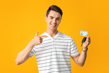 Young man with driving license and car key on color background