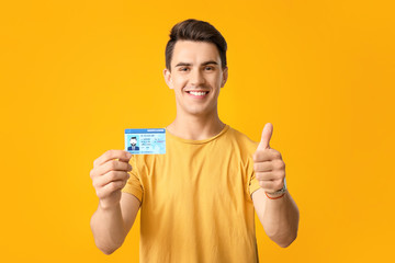 Young man with driving license showing thumb-up on color background