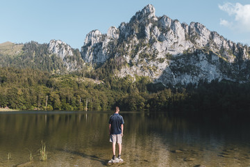 Fototapeta na wymiar Young man standing on rock in Laudachsee with alps mountain. Summer Austria landscape
