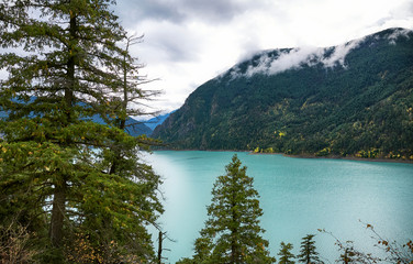 Obraz premium Turquoise mountain Carpenter lake in autumn. Fog on the tops of mountains with coniferous forest. Autumn forest landscape. BC, Canada