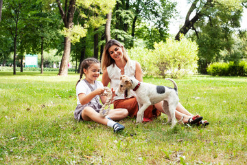 young pretty caucasian mother walking with little cute daughter and dog fox terrier, lifestyle people concept