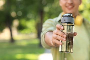 Young man with bottle of water in park, closeup