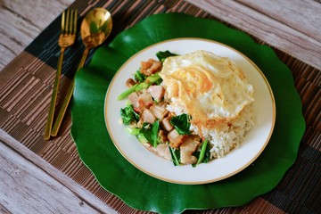 Stir-fried kale vegetable oyster sauce with crispy pork with fried egg top on rice and the plate. 