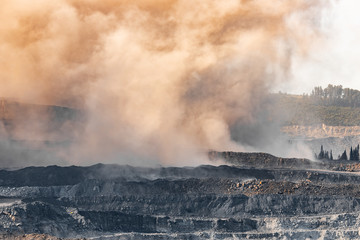 Explosive works on open pit coal mine industry. Dust and puffs of smoke in sky, blasted soil