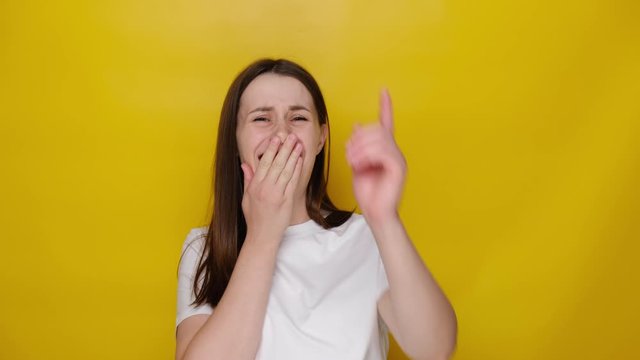 Amused happy millennial young woman isolated on yellow studio background pointing finger at camera and laughing out loud, holding belly with hilarious laughter, making fun of ridiculous appearance.