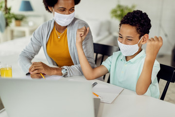 Happy black boy celebrating while using laptop and e-learning at home during virus pandemic.