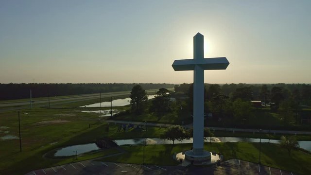 Rising shot of sunset behind Cross with landscape in view.