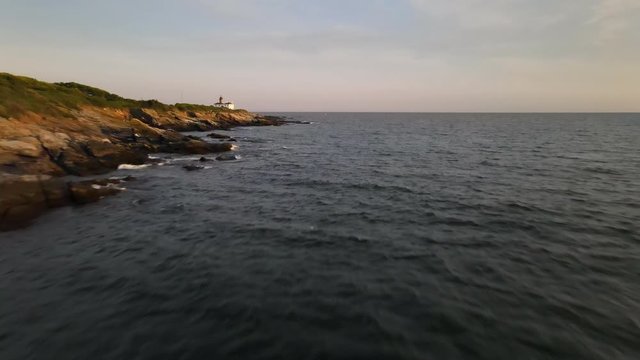 Aerial track over coastal rocks and lighthouse in New England
