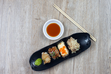 Top view of Japanese sushi Thai style in a black plate with soy sauce and wasabi on wooden table.
