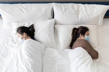 Asian people wearing medical protective face masks while sleep in a bed at safety distance to protect themselves and others or the family,prevent the spread of Coronavirus or COVID-19 after lockdown