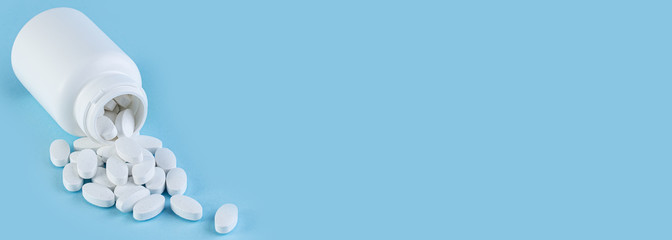 Pills spilling out of white bottle on blue background with copy space. Pharmaceutical medicament,...