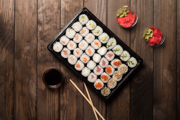 Sushi rolls in a plate on a wooden table with copy space. Next is red ginger root and soy sauce. Traditional Asian cooking concept.