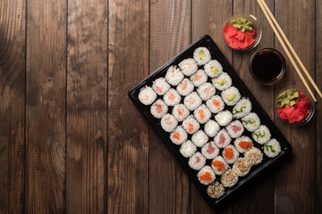 Sushi rolls in a plate on a wooden table with copy space. Next is red ginger root and soy sauce. Traditional Asian cooking concept.