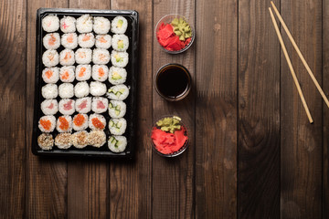 Sushi rolls in a plate on a wooden table with copy space. Next is red ginger root and soy sauce. Traditional Asian cooking concept.