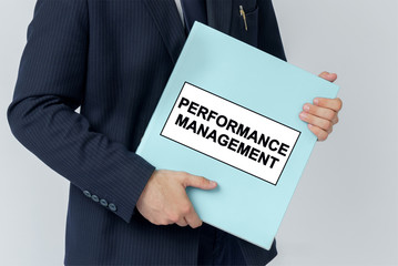 A businessman holds a folder with documents, the text on the folder is - PERFORMANCE MANAGEMENT